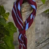 A burgundy and blue striped scarf tied loosely around a weathered wooden fence post. Green ivy leaves frame the left side. The background is soft and blurred. The mood is still and unhurried.